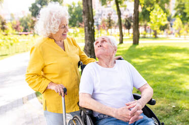 Beautiful senior couple with disability outdoors - Old people in the age of 60, 70, 80 having fun and spending time together, concepts about elderly, seniority, healthcare and wellness aging - DMDF02115