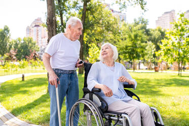 Beautiful senior couple with disability outdoors - Old people in the age of 60, 70, 80 having fun and spending time together, concepts about elderly, seniority, healthcare and wellness aging - DMDF02120