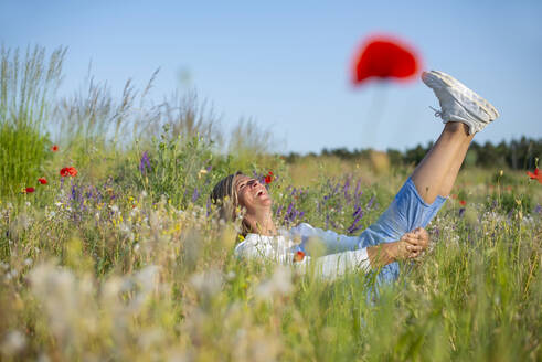 Playful woman having fun amidst flowers in meadow - BFRF02436