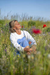 Woman with eyes closed sitting in meadow - BFRF02437