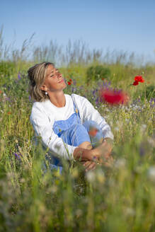 Woman with eyes closed sitting in meadow - BFRF02437
