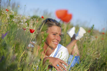Lächelnde Frau, die inmitten von Blumen auf einer Wiese liegt - BFRF02439