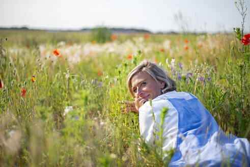 Smiling woman looking over shoulder lying down in meadow - BFRF02440