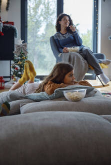 Mädchen auf Kissen liegend bei der Mutter mit Popcorn zu Hause - IKF01087