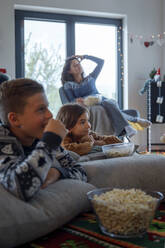 Geschwister sehen mit der Mutter fern und essen Popcorn zu Hause - IKF01088