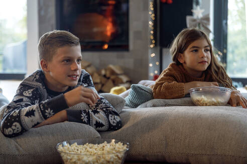 Bruder und Schwester essen Popcorn und sehen im Wohnzimmer fern - IKF01090