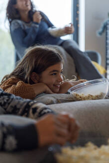 Smiling girl watching TV with mother and brother at home - IKF01096