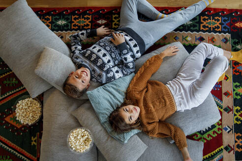 Bruder und Schwester liegen auf Kissen über dem Teppich im Wohnzimmer - IKF01100