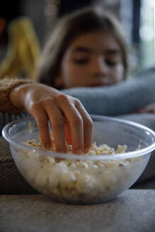 Girl taking popcorn from bowl at home - IKF01107