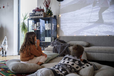 Brother and sister watching movie together in living room - IKF01110