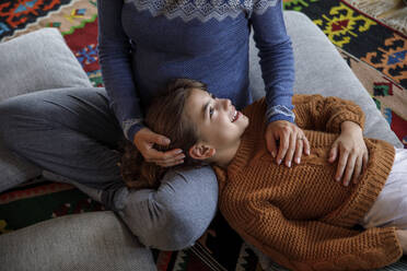 Smiling daughter resting head on mother's lap at home - IKF01115