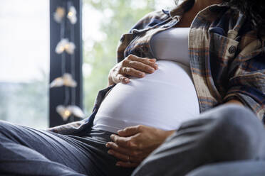 Schwangere Frau mit Händen auf dem Bauch zu Hause - IKF01121