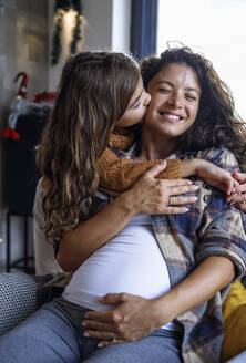 Mädchen küsst glückliche schwangere Mutter im Wohnzimmer - IKF01137