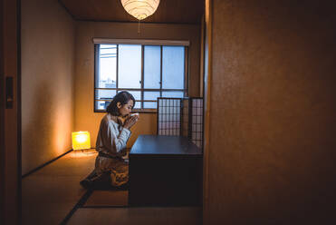 Japanese woman sitting in a traditional Tokyo apartment and drinking a cup of hot tea - DMDF02293