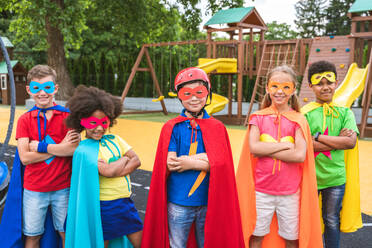 Eine gemischtrassige Gruppe junger Schüler trägt Superheldenkostüme und hat Spaß im Freien - DMDF02362