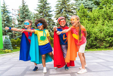 Eine gemischtrassige Gruppe junger Schüler trägt Superheldenkostüme und hat Spaß im Freien - DMDF02372