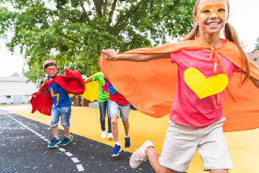 Eine gemischtrassige Gruppe junger Schüler trägt Superheldenkostüme und hat Spaß im Freien - DMDF02422
