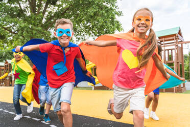 Eine gemischtrassige Gruppe junger Schüler trägt Superheldenkostüme und hat Spaß im Freien - DMDF02423