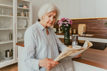 Senior woman relaxing at home, reading newspaper and having breakfast - DMDF02452