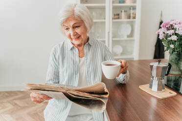 Senior woman relaxing at home, reading newspaper and having breakfast - DMDF02453