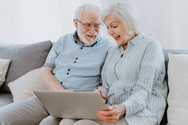 Elderly couple shopping online on internet with computer laptop at home - Beautiful happy senior people using pc and social network apps - DMDF02476