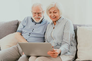 Elderly couple shopping online on internet with computer laptop at home - Beautiful happy senior people using pc and social network apps - DMDF02477