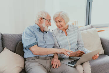 Elderly couple shopping online on internet with computer laptop at home - Beautiful happy senior people using pc and social network apps - DMDF02479