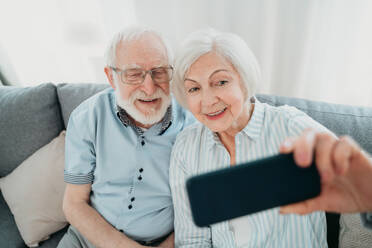 Happy senior couple having fun and taking photograph on mobile phone to share online on social networks - Elderly people using modern technology, grandparents taking selfie - DMDF02480
