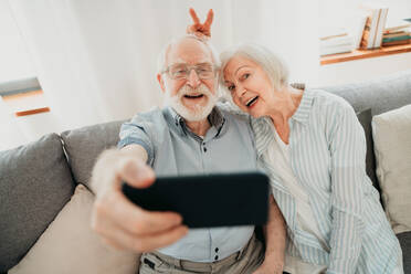 Happy senior couple having fun and taking photograph on mobile phone to share online on social networks - Elderly people using modern technology, grandparents taking selfie - DMDF02481