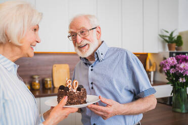 Schönes älteres Paar feiert Jahrestag mit Geburtstagstorte - Älteres Paar feiert Geburtstagsparty zu Hause - DMDF02513
