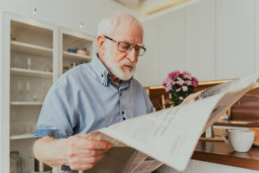 Senior man relaxing at home, reading newspaper and having breakfast - DMDF02530