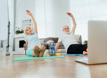 Sportive senior couple doing fitness and relaxation exercises at home - Elderly people training to stay healthy and fit - DMDF02535