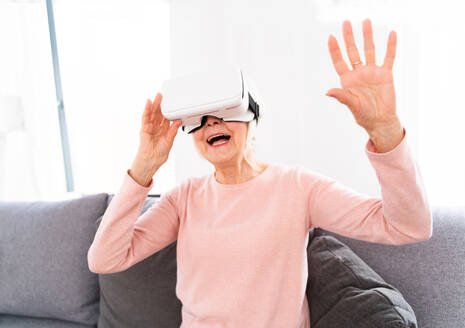 Beautiful elderly woman with vr googles at home - Mature woman playing with virtual reality world - DMDF02551