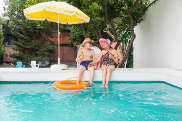 Happy senior couple having party in the swimming pool - Elderly friends releaxing at a pool party during summer vacation - DMDF02558