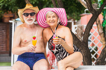 Happy senior couple having party in the swimming pool - Elderly friends releaxing at a pool party during summer vacation - DMDF02560