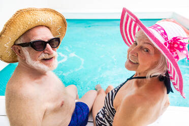 Happy senior couple having party in the swimming pool - Elderly friends releaxing at a pool party during summer vacation - DMDF02568