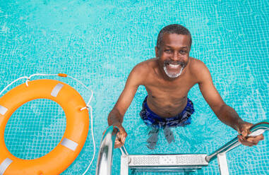 Happy senior man having party in the swimming pool - Active elderly male person sunbathing and relaxing in a private pool during summertime - DMDF02569