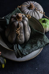 High angle of autumnal table setting with napkin and black pumpkin placed on ceramic bowl near green pumpkins against dark surface - ADSF46581