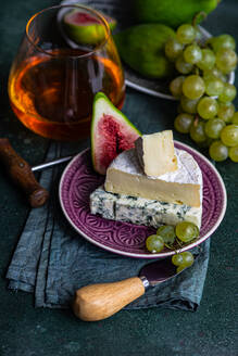 Assorted yummy snacks with cheese and served on plate placed with grapes and figs and drink - ADSF46584