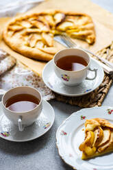 High angle of plates with pieces of apple pie and cups of tea served on rustic tray against gray table - ADSF46586