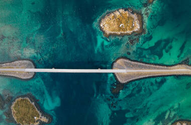 From above aerial view of Lofoten bridge and road surrounded by transparent blue river and rocky Henningsvaer archipelago in daytime - ADSF46613