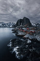 Scenic view of rough rocky snowy mountains and ocean with horizon under cloudy evening sky in Henningsvaer archipelago Lofoten Norway - ADSF46614