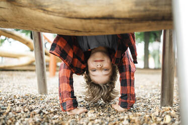 Smiling boy playing on outdoor play equipment in park - ANAF01933