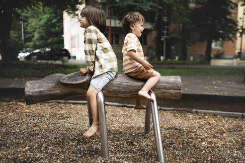 Verspielte Jungen sitzen auf Spielgeräten im Park - ANAF01936