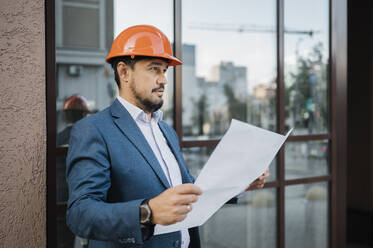 Thoughtful engineer holding document in front of building - ANAF01940