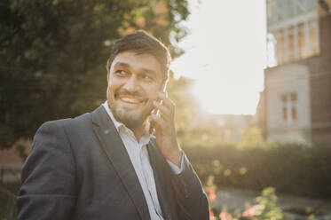 Smiling businessman talking on smart phone in park - ANAF01942