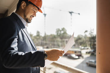 Engineer reading document in balcony on sunny day - ANAF01943