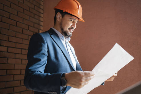 Engineer wearing hardhat reading and document at construction site - ANAF01944