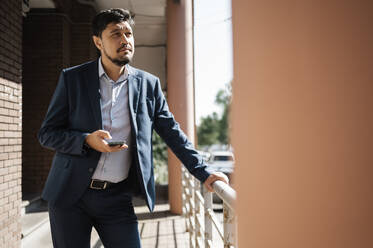 Contemplative businessman standing in office balcony - ANAF01945