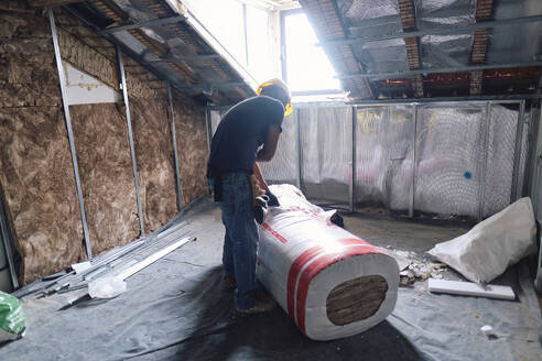 Mature construction worker with insulation roll working on site - ASGF04291